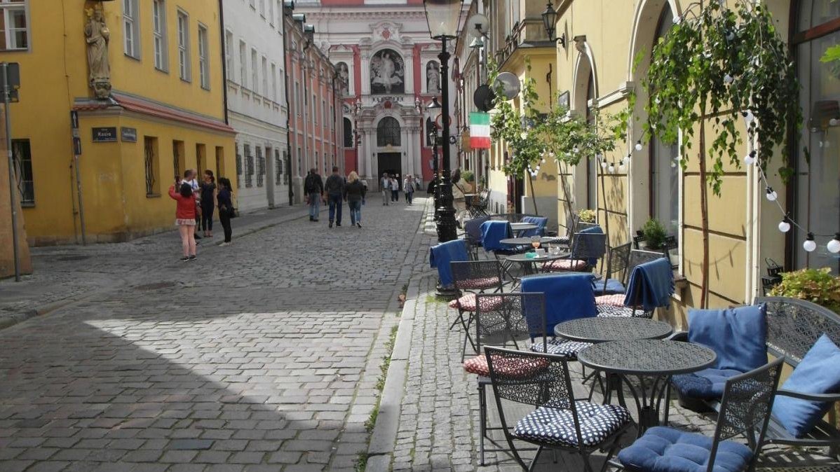 Zdjęcie: na pierwszym planie ogródek gastronomiczny, na krzesłach wiszą niebieskie koce. W tle poznańska fara