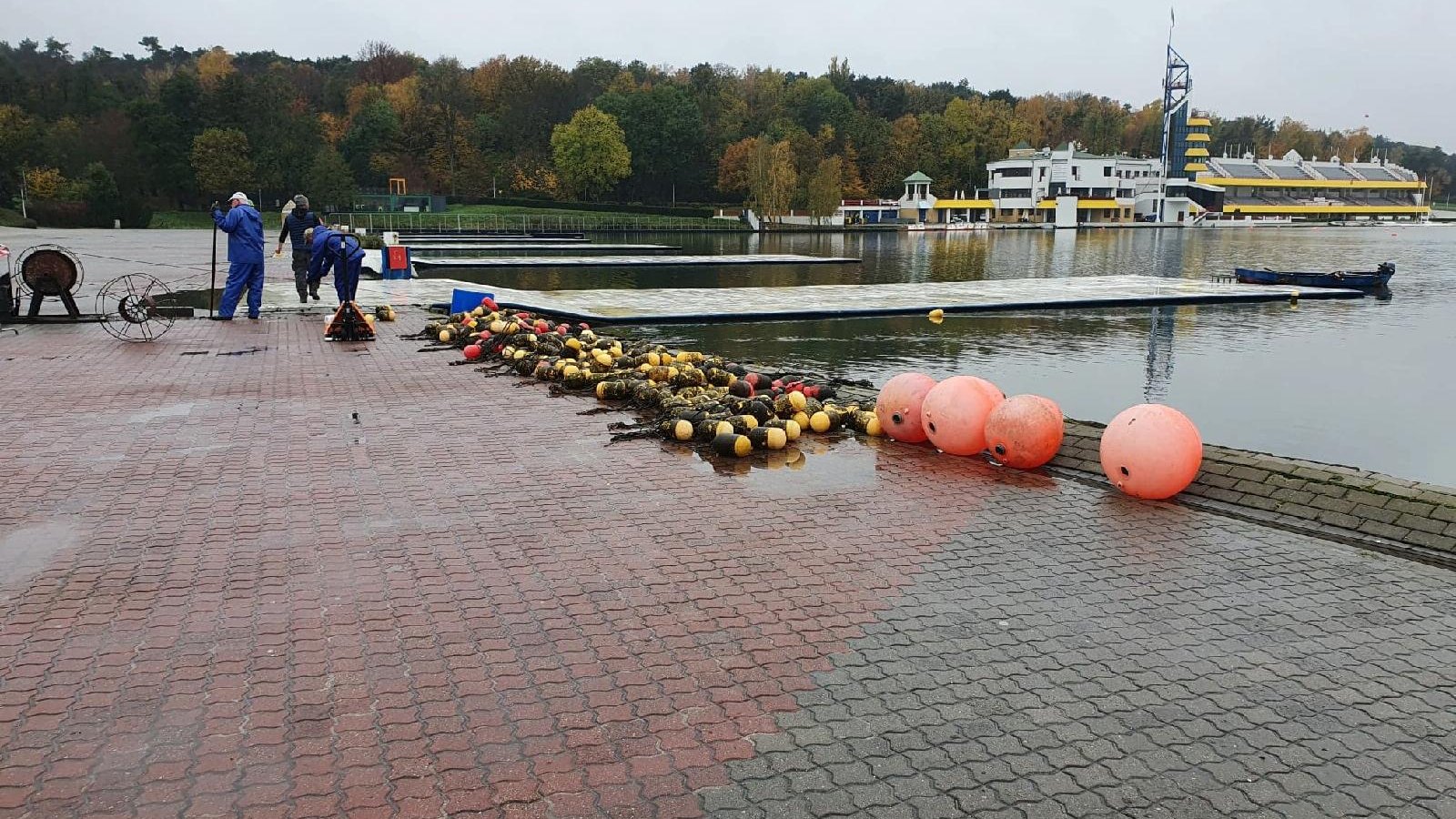 Jezioro Maltańskie - pracownicy wyciągają na brzeg boje. W tle widać trybuny oraz drzewa.