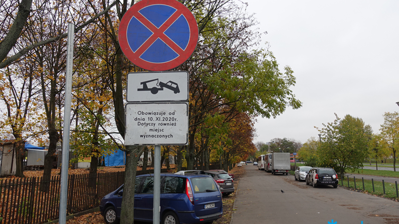 Znaki informujące o zakazie zatrzymywania i zaparkowane samochody w okolicach targowiska.