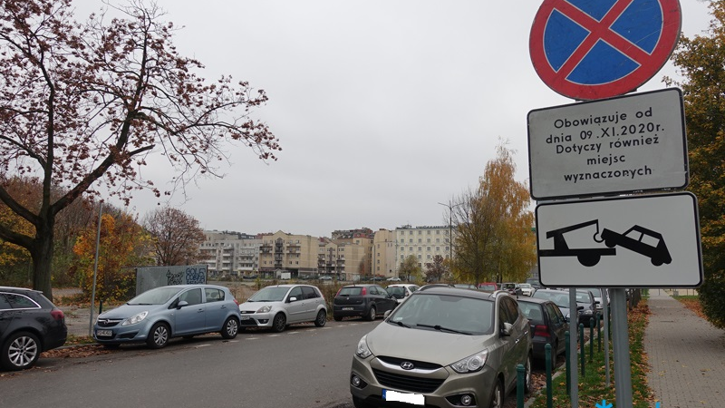 Znaki informujące o zakazie zatrzymywania i zaparkowane samochody w okolicach targowiska.