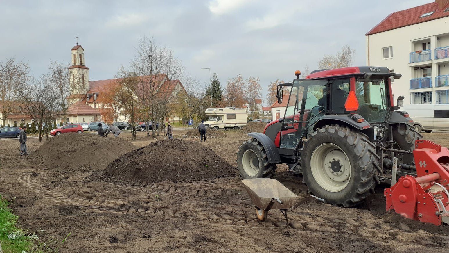 Na piertwszym planie ciągnik. W tle ludzie, w oddali kościół.