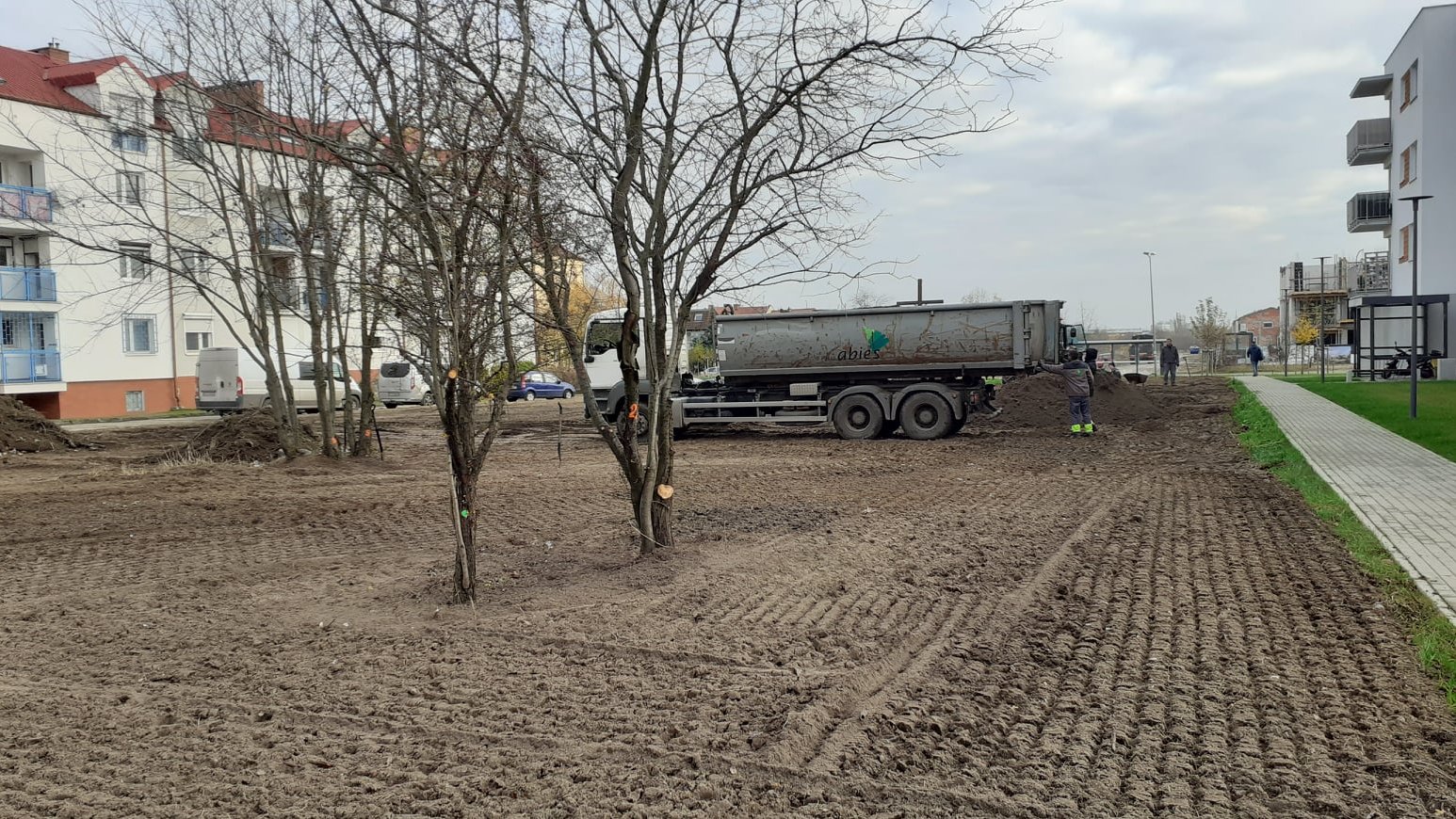 Rozkopana ziemia. W tle osiedle mieszkaniowe i ciężarówka.