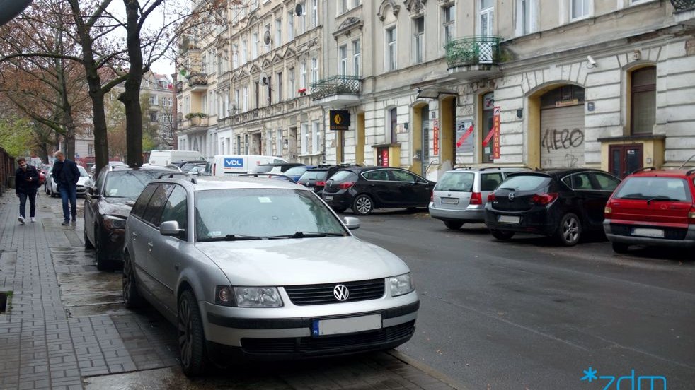 Ulica Łąkowa z zaparkowanymi samochodami i znakiem drogowym