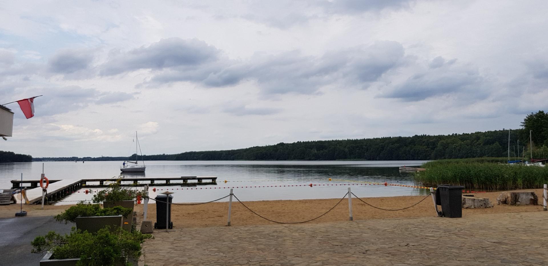 Zdjęcie przedstawia miejską plażę. Na jeziorze widać pomost i statek. - grafika artykułu