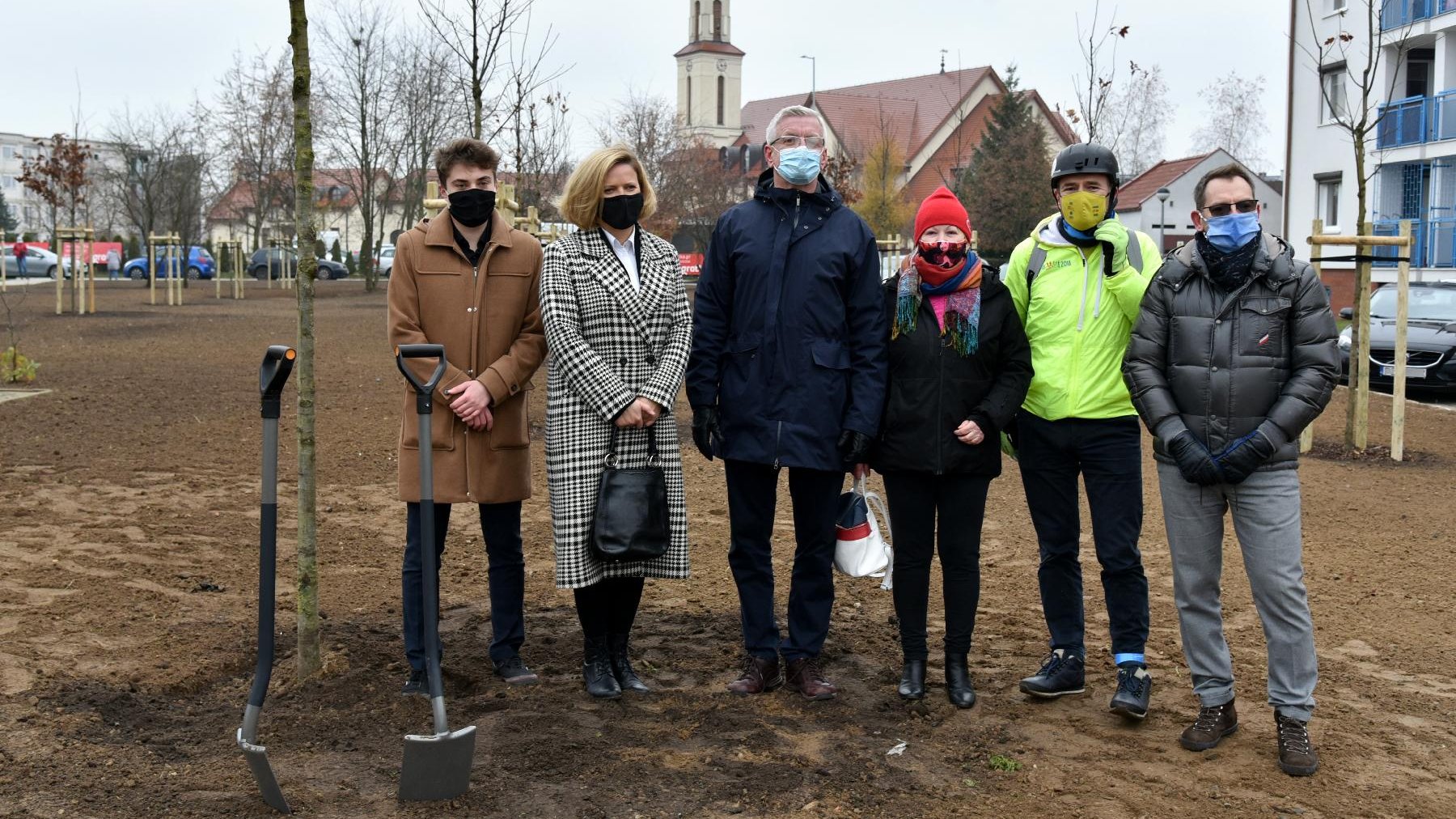 Grupa ludzi na pierwszym planie, w tle kościół i drzewa.