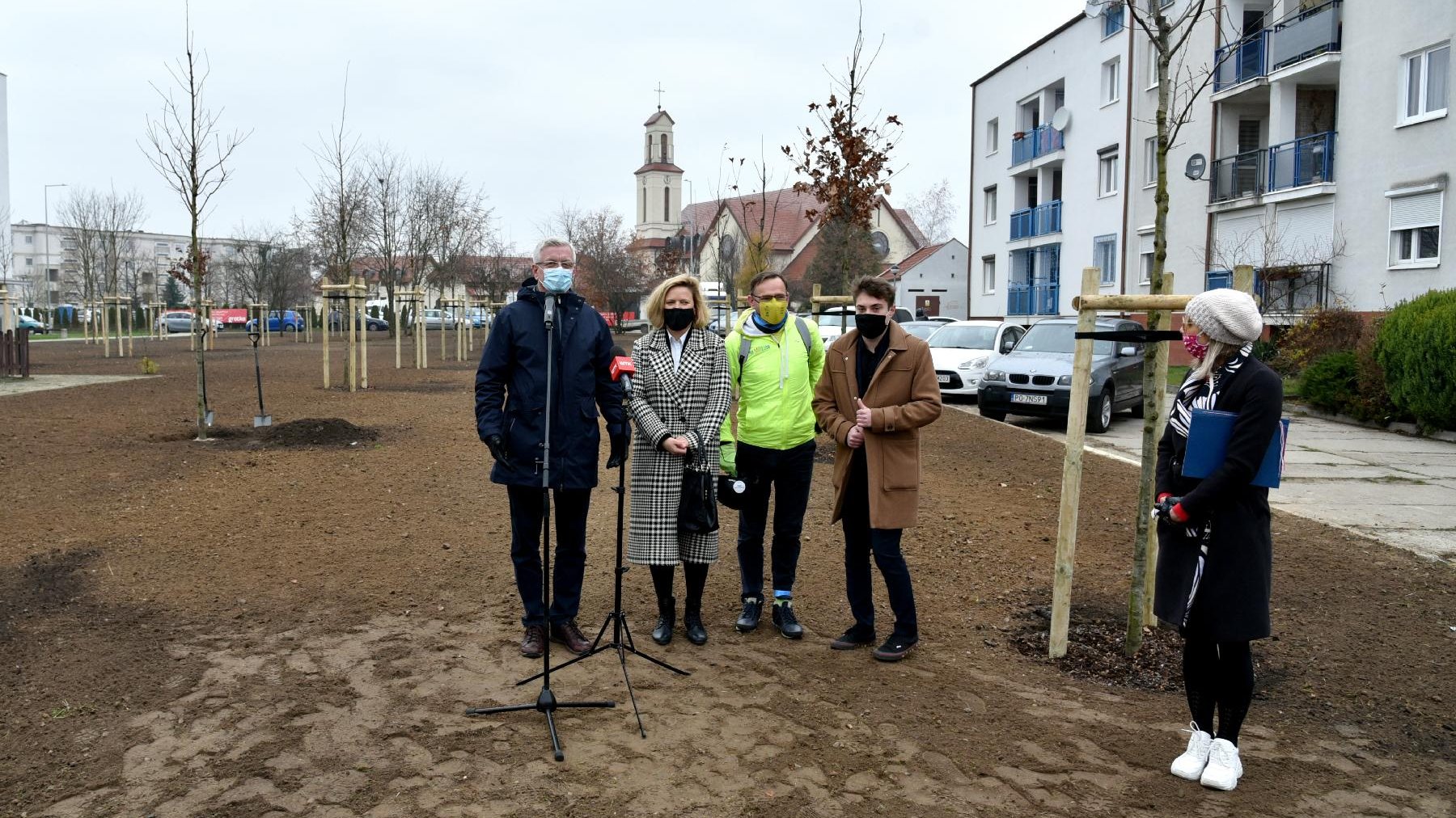 Grupa ludzi na pierwszym planie, w tle kościół i drzewa.