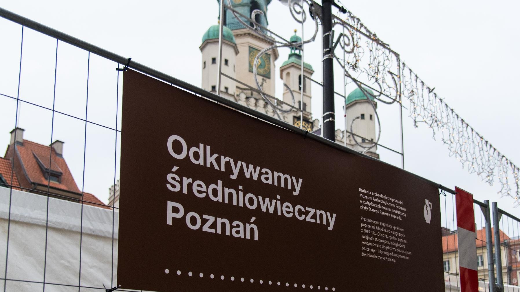 Tablica z napisem "Odkrywamy średniowieczny Poznań". W tle wieża Ratusza.