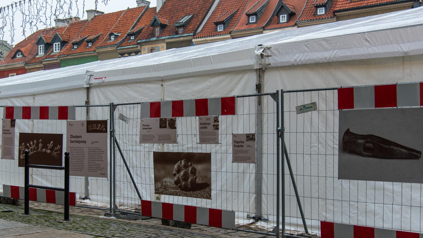 Tablice wystawy "Odkrywamy średniowieczny Poznań", na nich zdjęcia artefaktów i opisy. W tle namiot archologów.