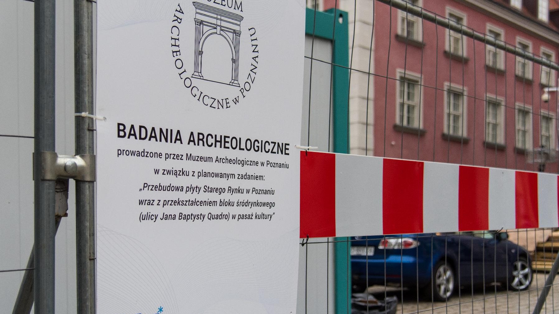 Tablica z napisem "Badania archeologiczne". W tle domki budniczne.