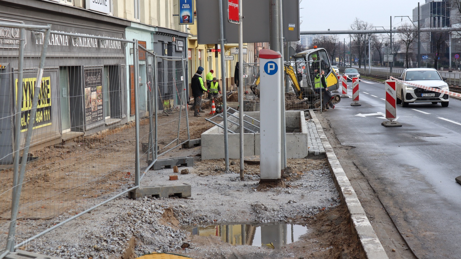 Pracownicy budowlani układają nawierzchnię chodnika. Na zdjęciu widać też jezdnię i samochody. - grafika artykułu