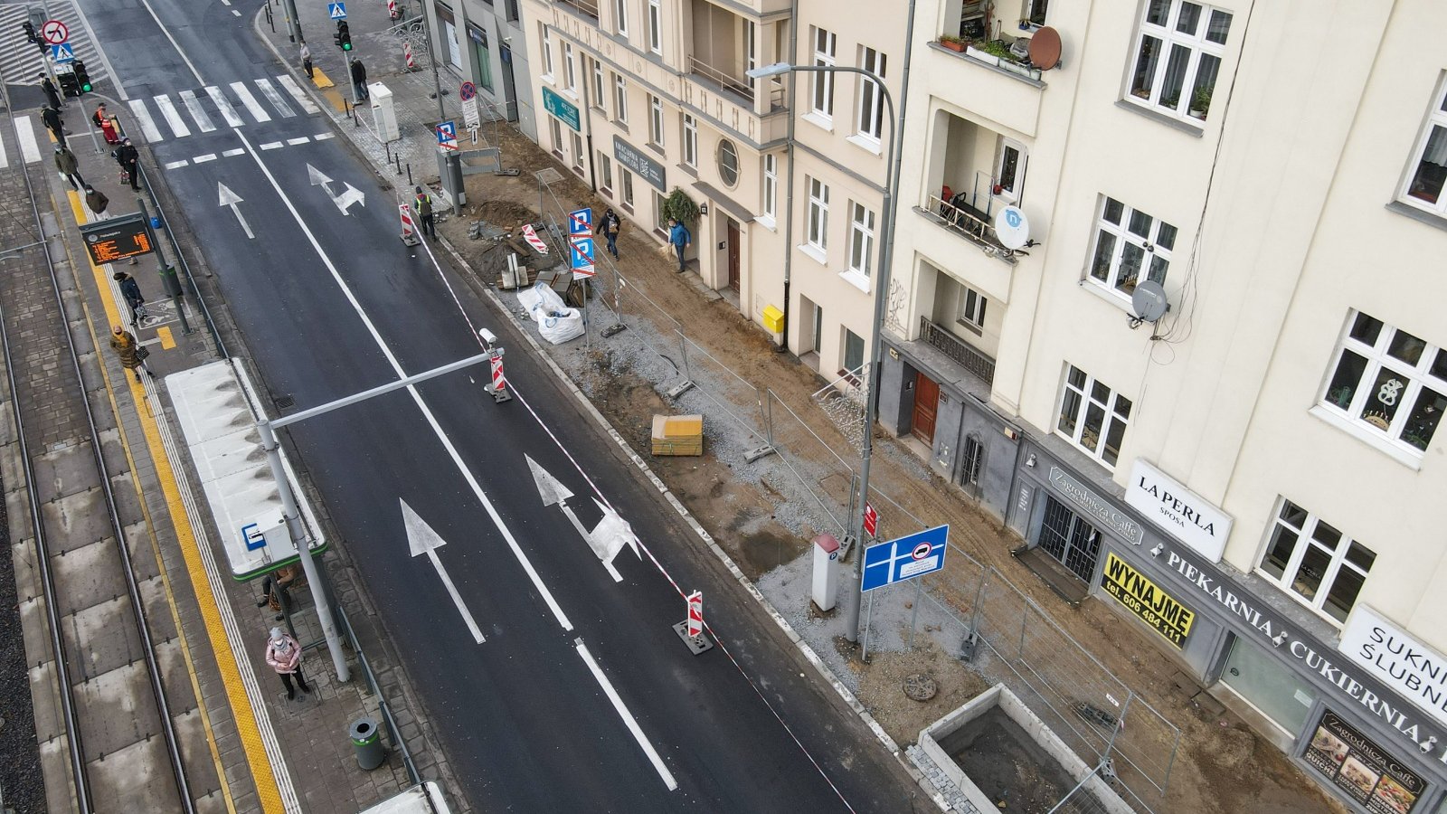 Prace nad budową nowego chodnika. Zdjęcie z góry. Widać na nim też jezdnię, pieszych i sąsiedni budynek.