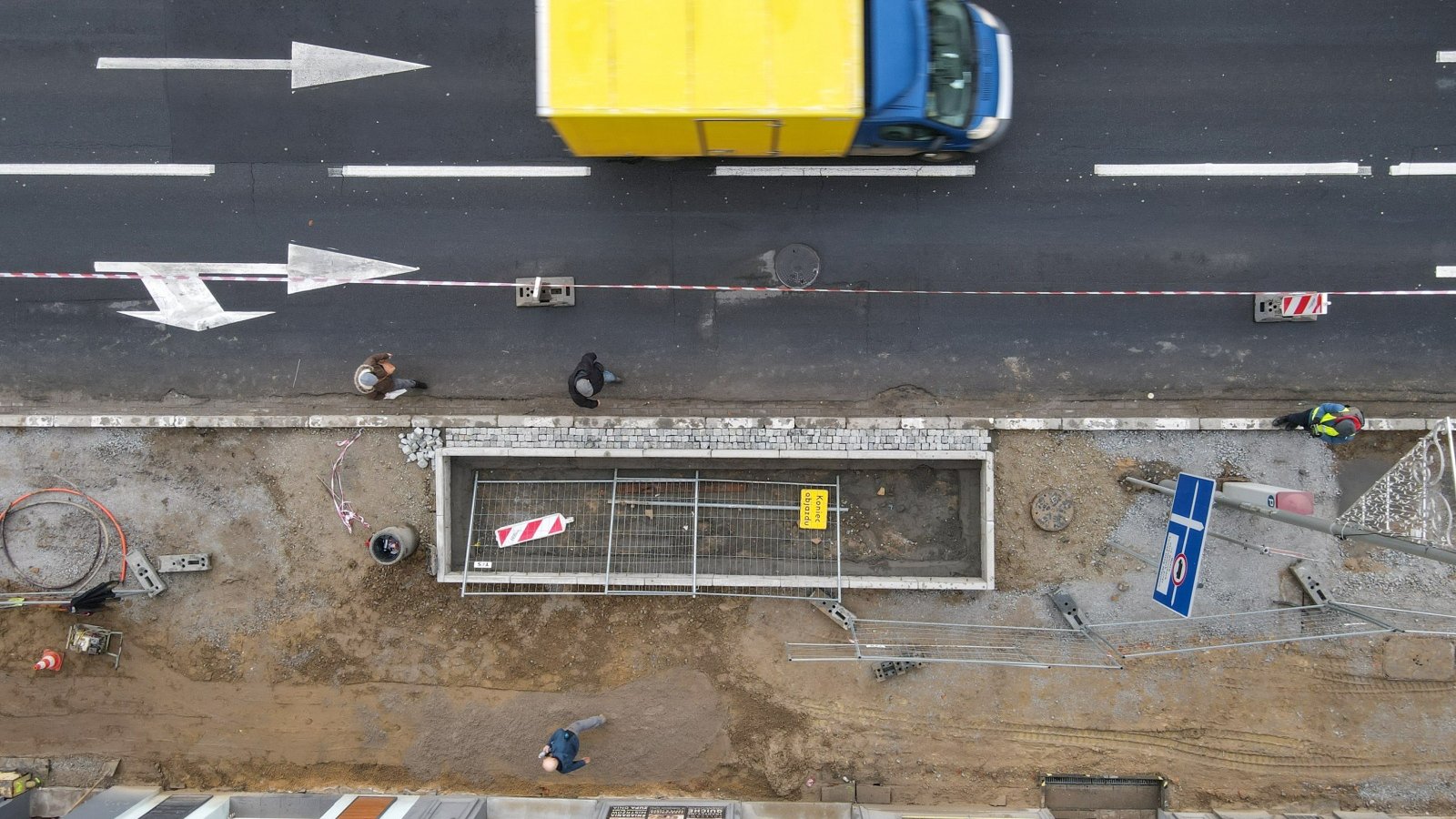 Prace nad budową nowego chodnika. Zdjęcie z góry. Widać na nim też jezdnię, pieszych i samochód dostawczy.