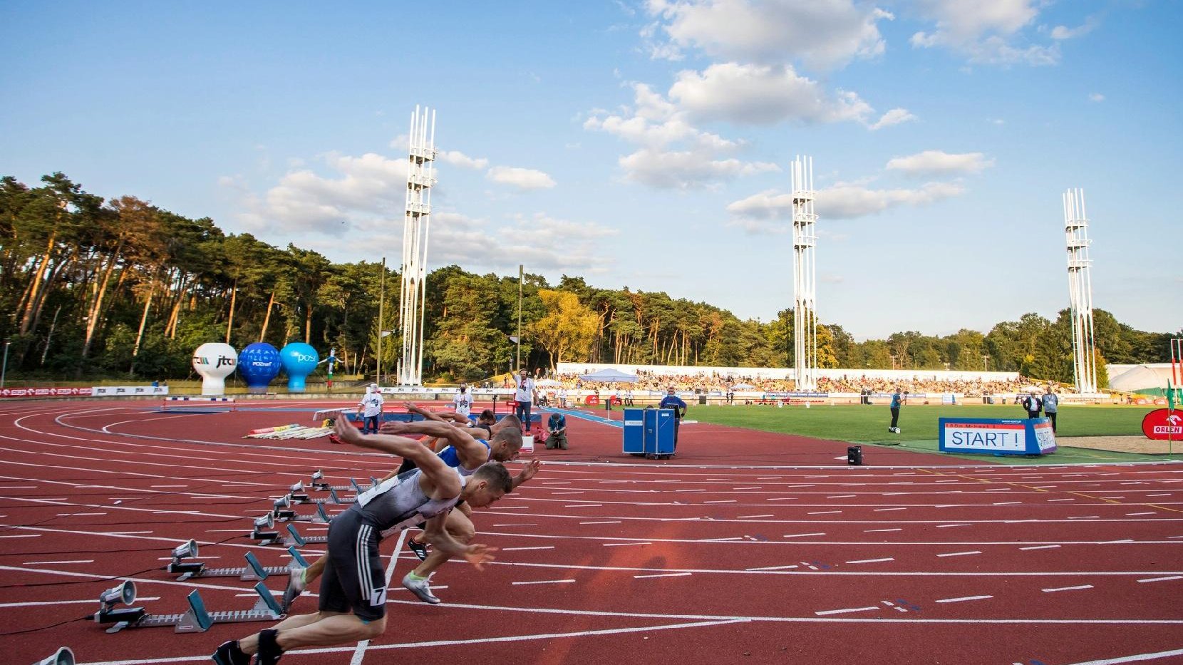 Zdjęcie przedstawia biegnących po torze mężczyzn. Fotografia została zrobiona na stadionie na Golęcinie.