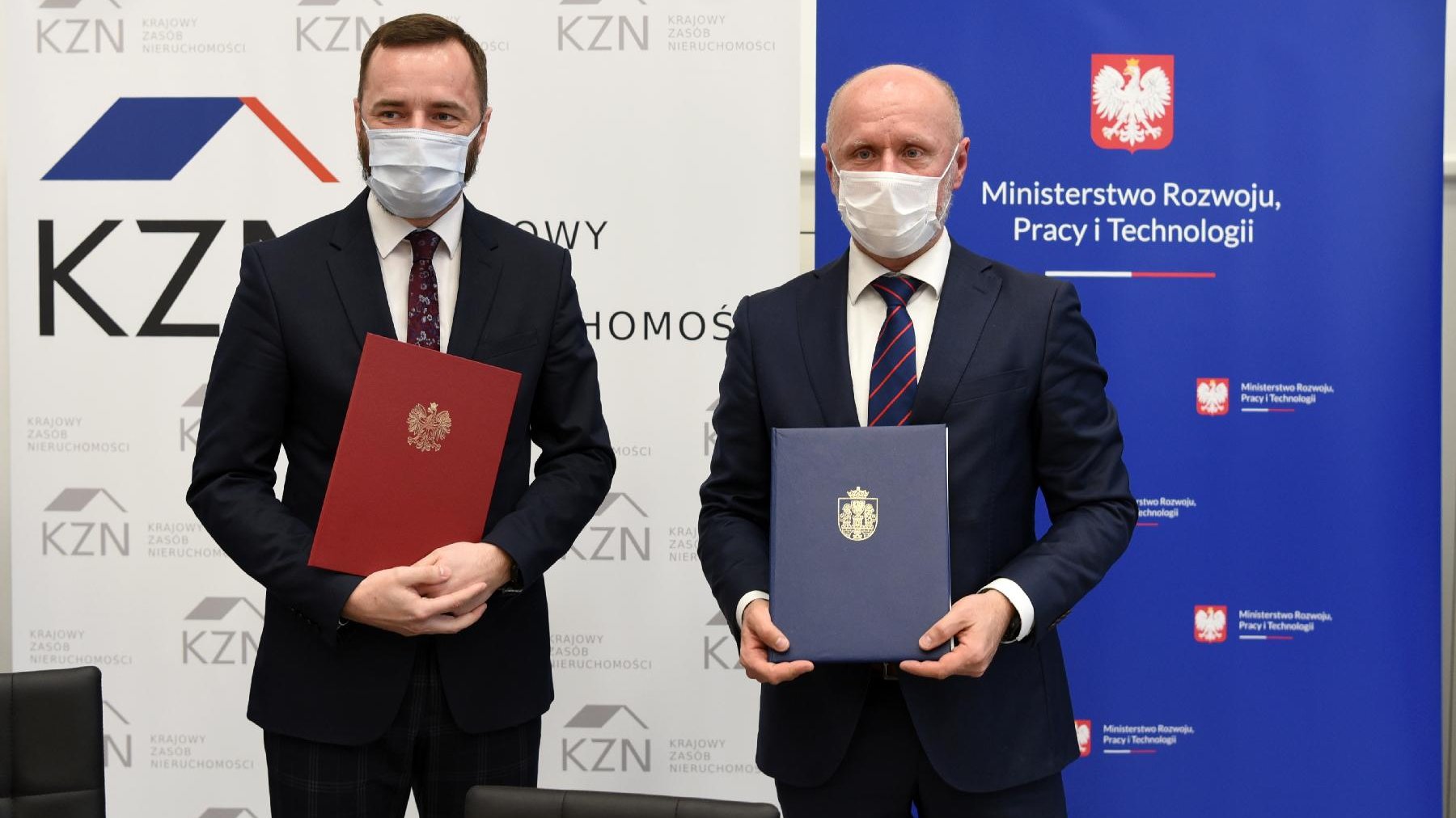 Bartosz Guss i Jarosław Pucek, obaj w maseczkach, stoją obok siebie, trzymając teczki z dokumentami