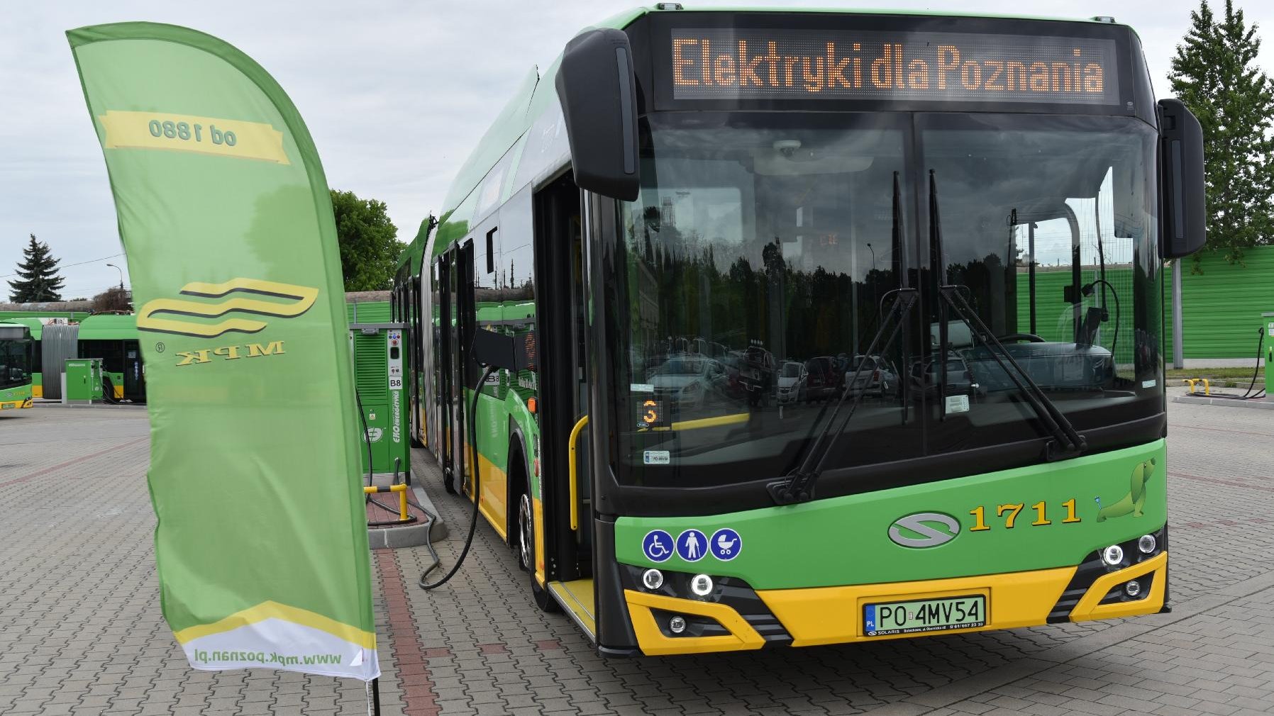 Na zdjęciu elektryczny autobus przed zajezdnią, nad przednią szybą ma napis: Elektryki dla Poznania