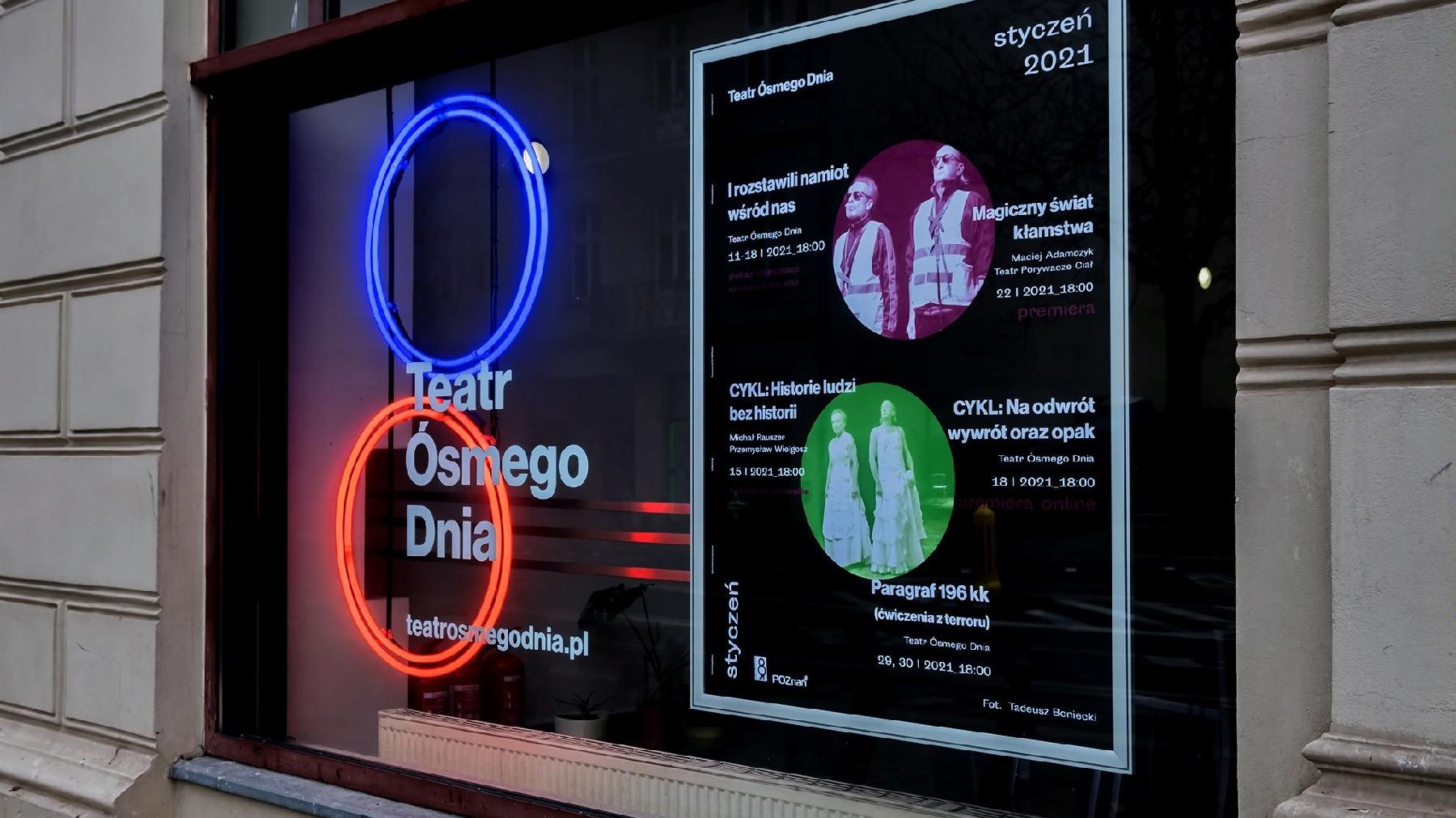 Zdjęcie przedstawia wejście do Teatru Ósmego Dnia. Na szybie okna znajduje się neon - czerwony i niebieski okrąg oraz plakat z repertuarem na styczeń.