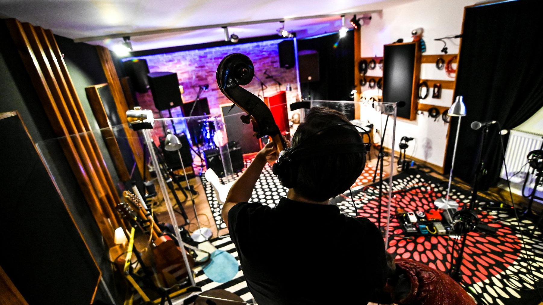 Studio nagrań. Na pierwszym kontrabasista odwrócony plecami do zdjęcia. W tle różnego rodziaju instrumenty, wzmancniacz, mikrofony.