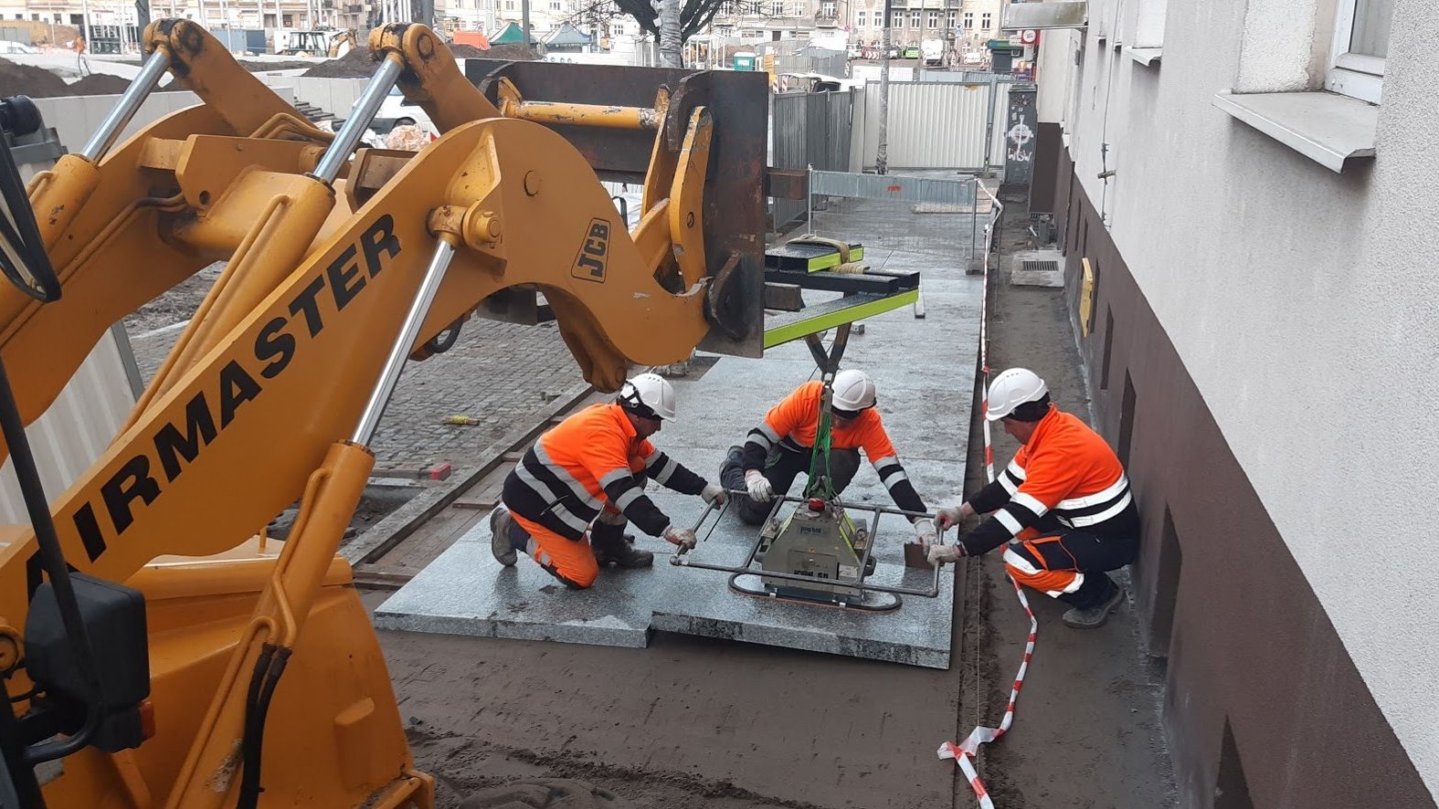 Na zdjęciu Rynek Łazarski - na pierwszym planie ramię maszyny, w tle - układający chodnik robotnicy