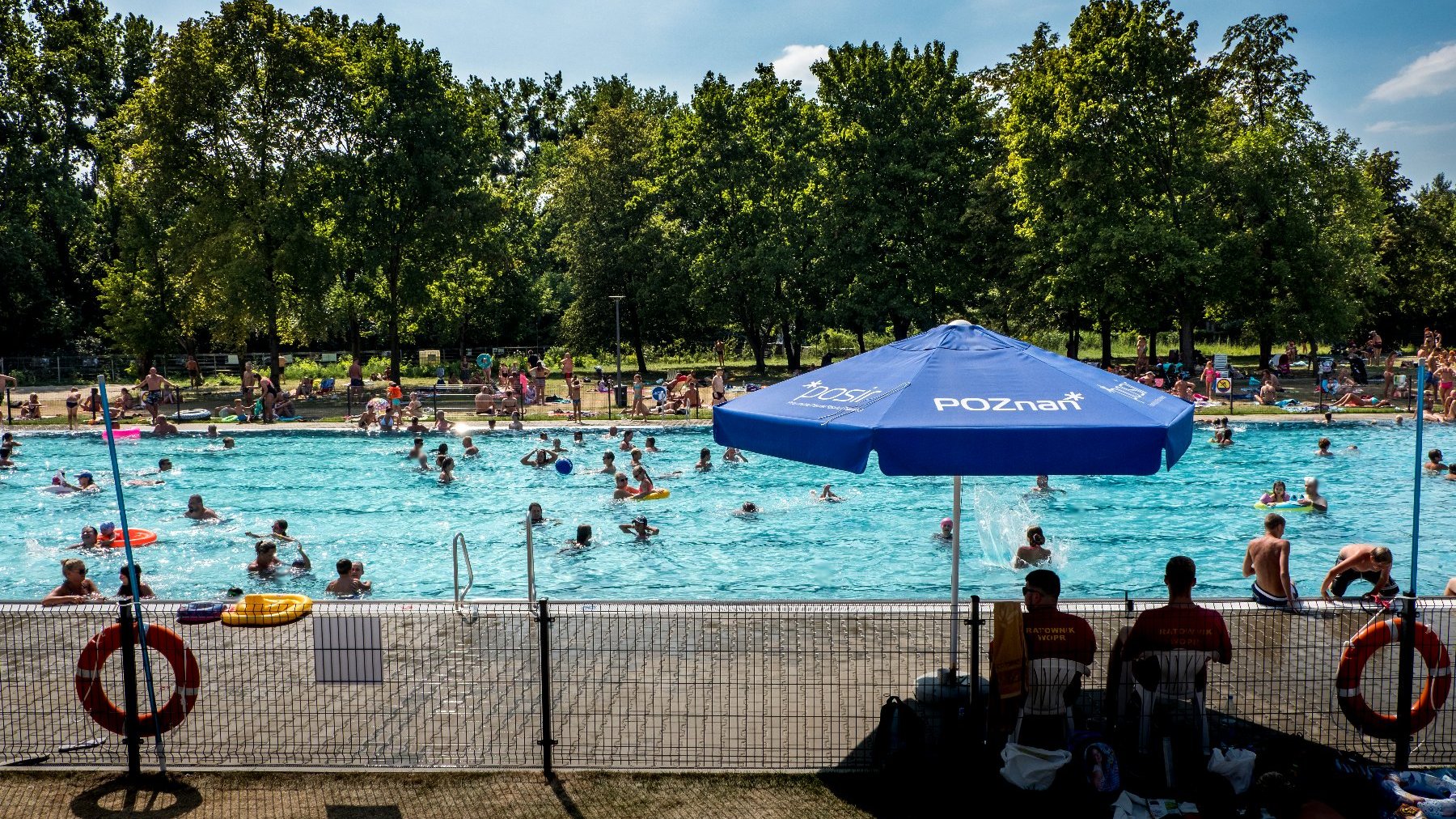 Basen zewnętrzny - w wodzie i na plaży znajduje się tłum ludzi.