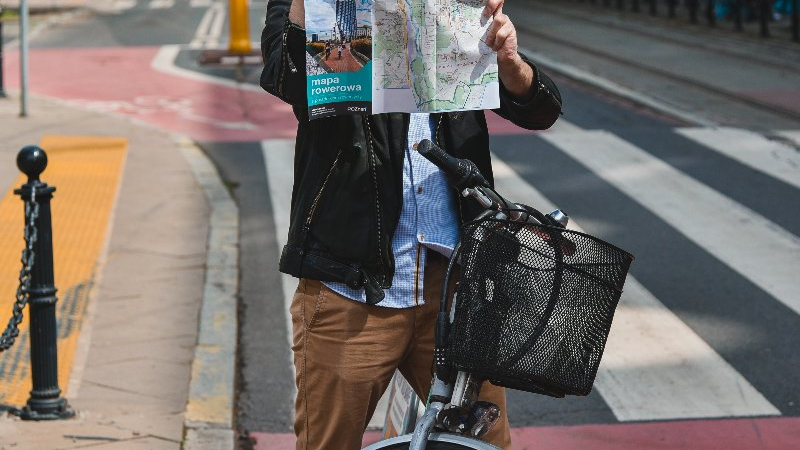 Mężczyzna na rowerze w centrum miasta, w rękach trzyma mapę