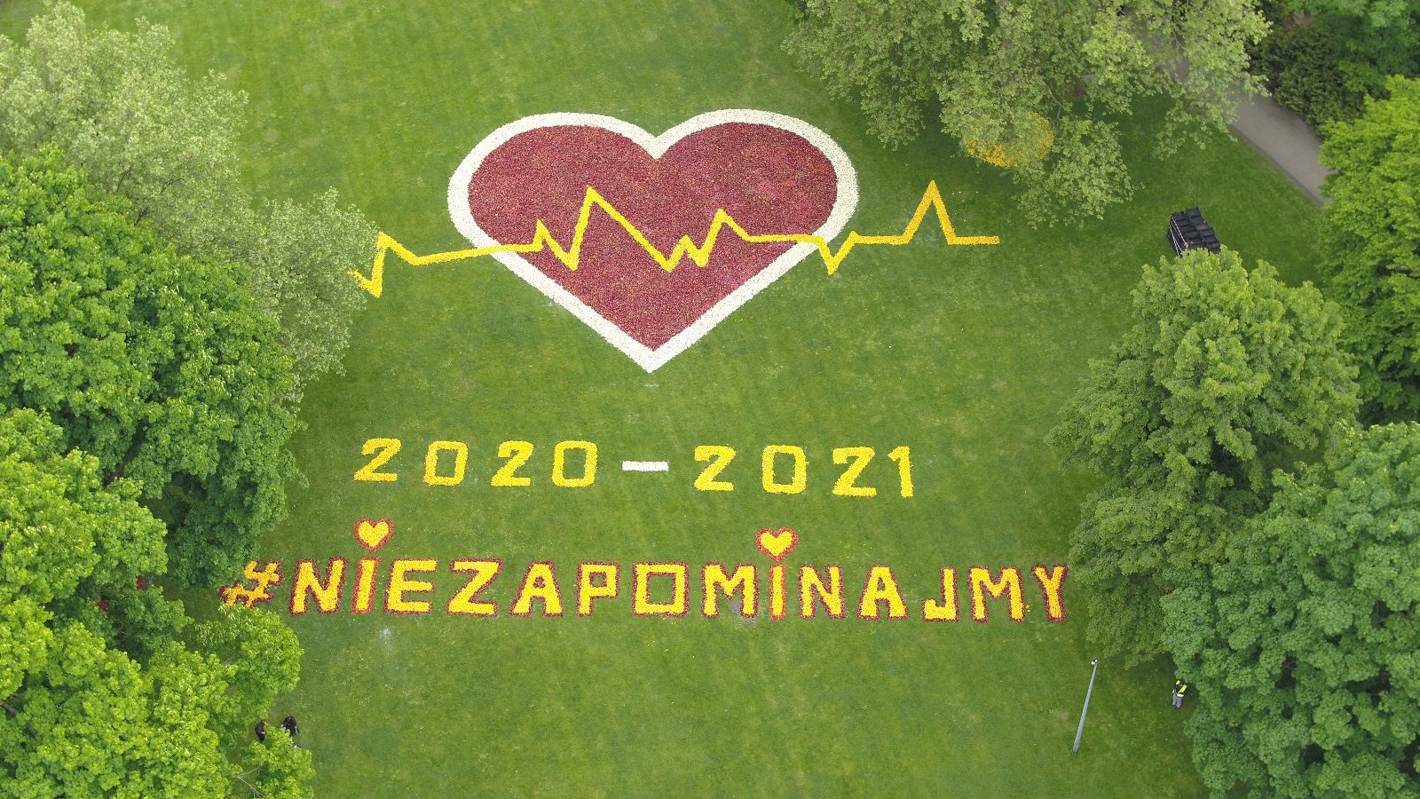 Zdjęcie przedstawia ułożone z kwiatów serce i napis "Nie zapominajmy" oraz lata 2020-2021. Fotografia została zrobiona z góry, za pomocą drona.