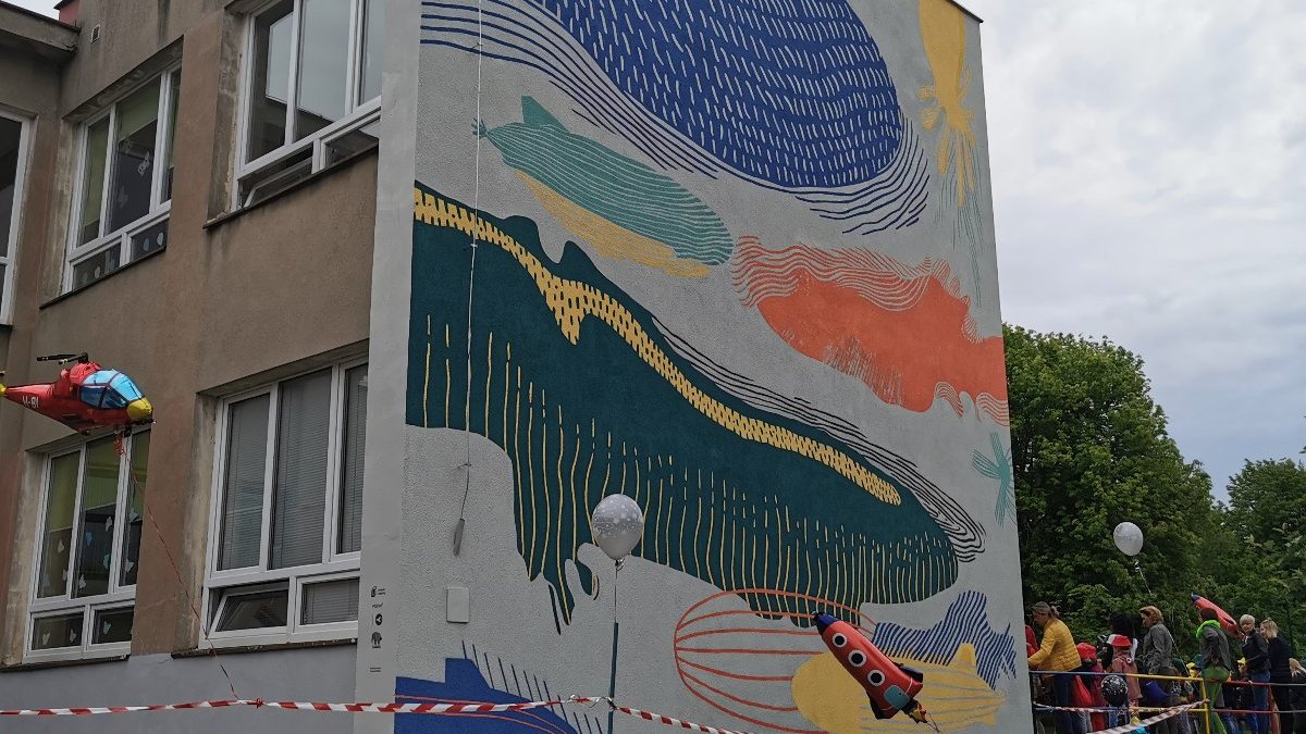 Zdjęcie przedstawia mural, po prawej strony widać dzieci i nauczycieli.