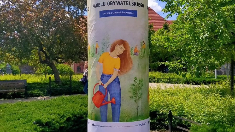 Zdjęcie przedstawia plakat na słupie ogłoszeń. W tle widać zieleń.