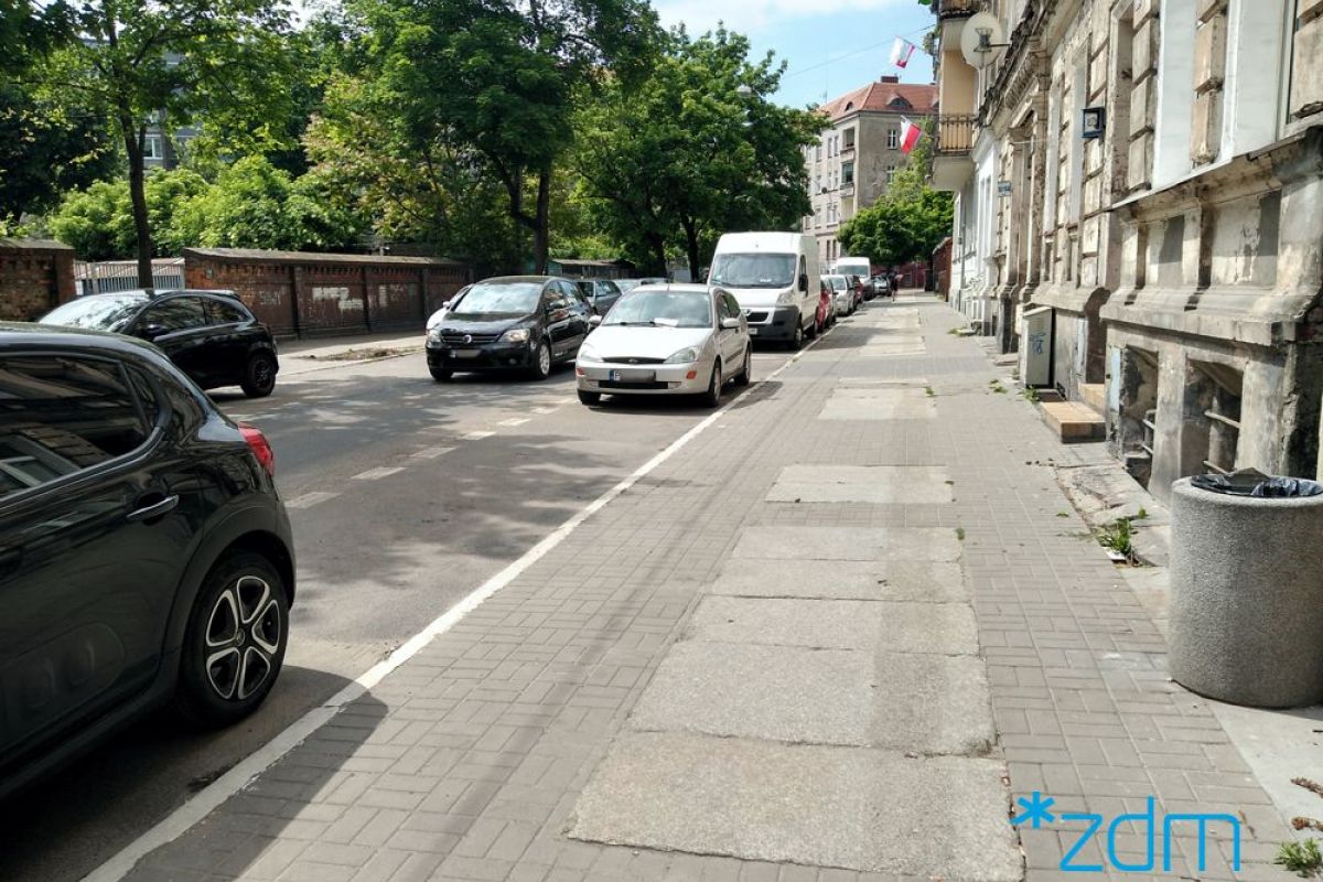 Zdjęcie przedstawia jezdnię i chodnik. Na poboczu drogi stoją zaparkowane samochody. - grafika artykułu