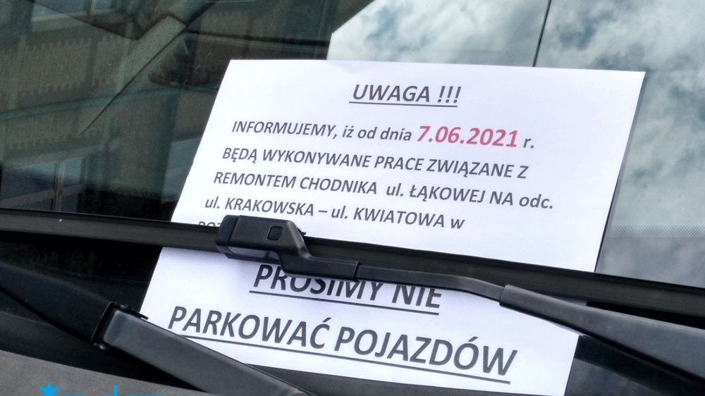 Zdjęcie przedstawia kartkę, na której znajdują się informacje o planowanych pracach, włożoną za wycieraczki samochodu.