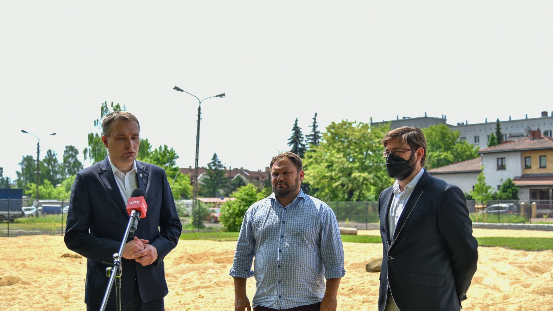 Zdjęcie przedstawia wiceprezydenta Wiśniewskiego, radnego Stachowiaka i dyrektora Zarządu Zieleni Miejskiej. Panowie stoją przy mikrofonie, na wybiegu dla psów.