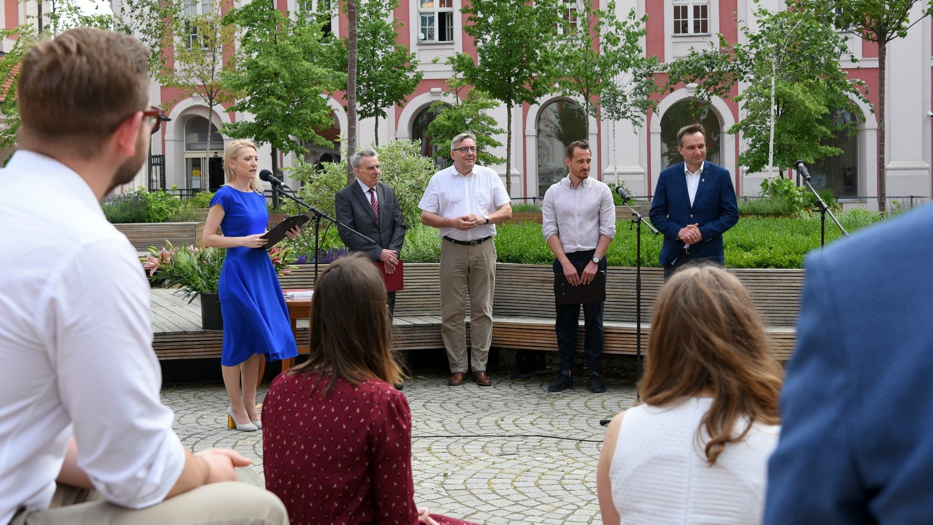 Dziedziniec Urzędu Miasta Poznania. Przy mikrofonach kobieta i czterech mężczyzn, wśród nich zastępca prezydenta Poznania i przewodniczący rady miasta