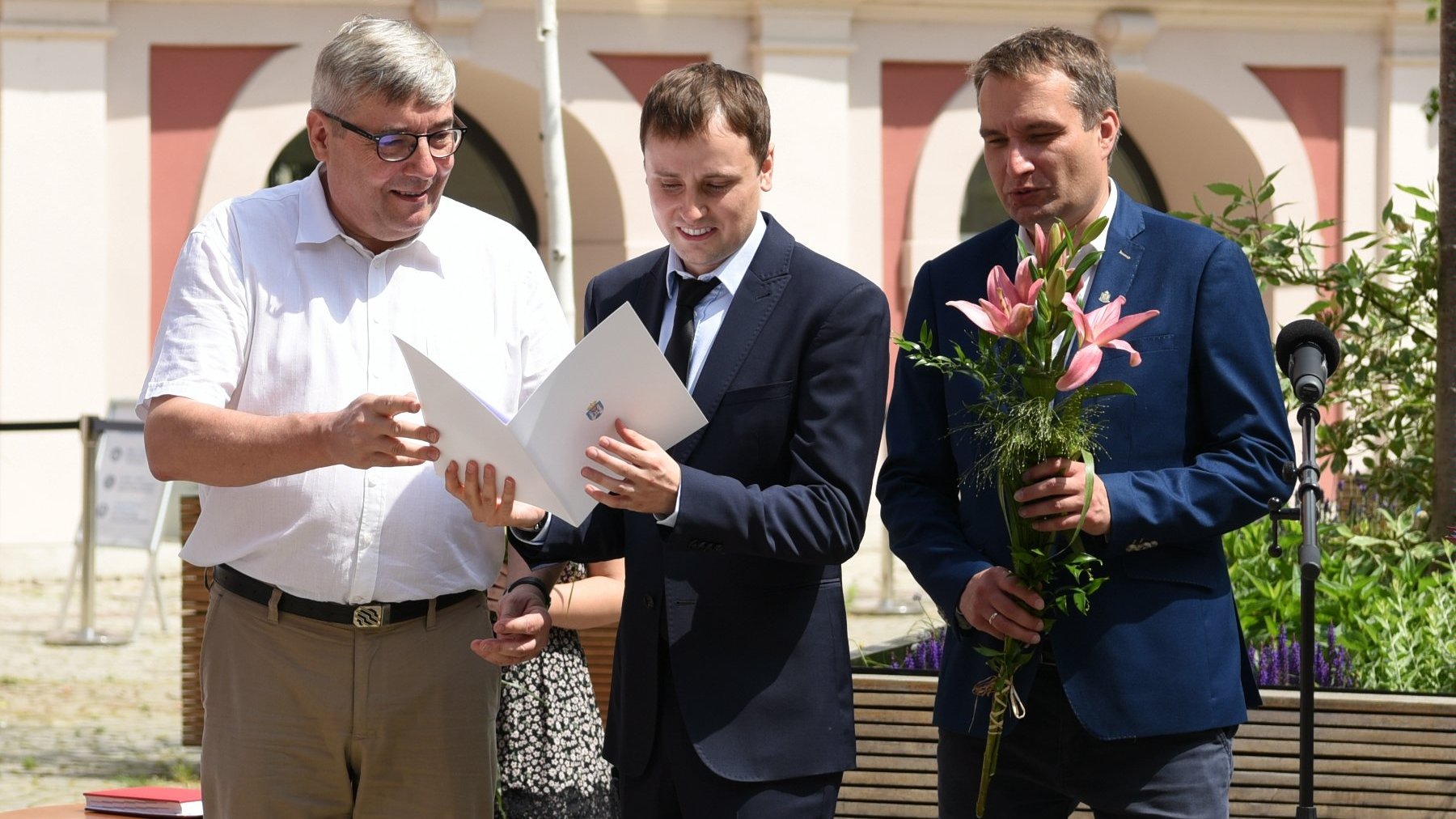 Dziedziniec Urzędu Miasta Poznania. Stypendysta trzymający w ręku teczkę, obok niego Grzegorz Ganowicz i Mariusz Wiśniewski