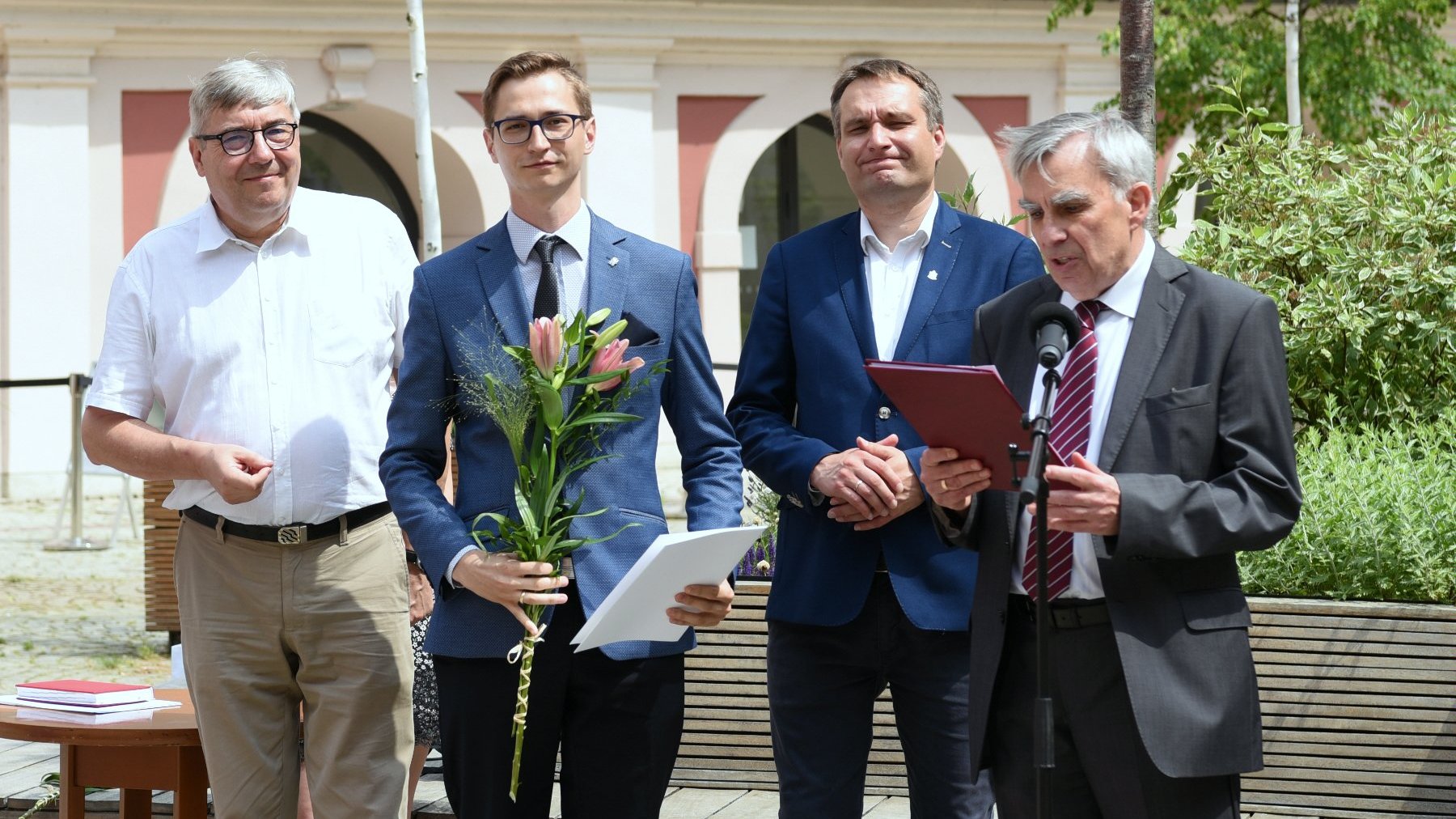 Dziedziniec Urzędu Miasta Poznania. Stypendysta trzymający w ręku kwiat, obok niego Grzegorz Ganowicz, Mariusz Wiśniewski i prof. Witold Jurek