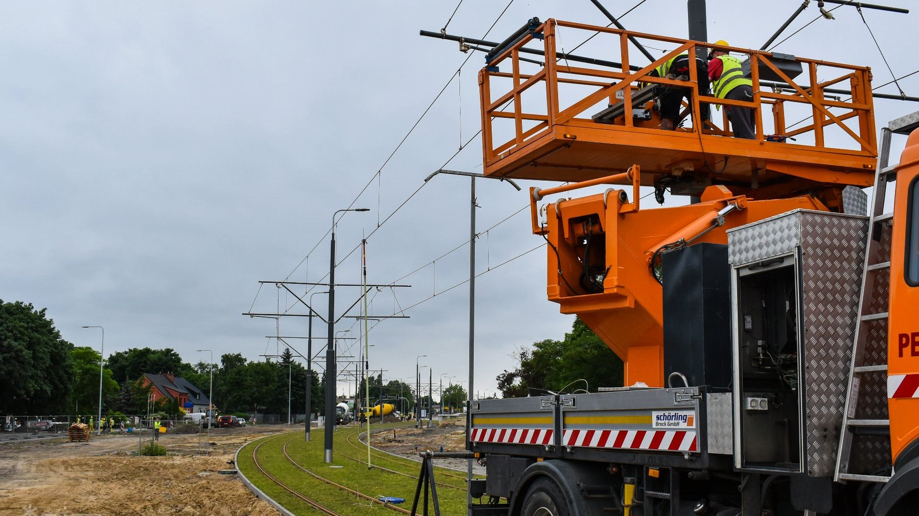 Na zdjęciu robotnicy w żółtym podnośniku, wykonujący prace przy słupie, w tle torowisko