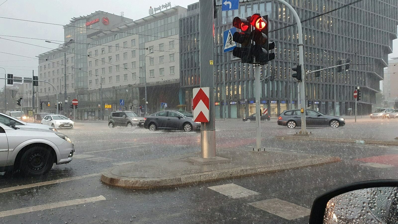 Zdjęcie przedstawia zalaną ulicę. Widać na nim samochody i budynki.