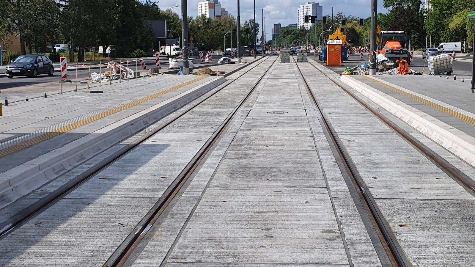 W centrum zdjęcia tory tramwajowe, po prawej stronie widać pracującego przy nich robotnika, w tle wieżowce