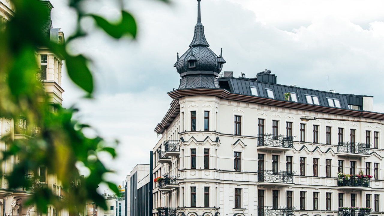 Kamienica "Żelazko" - biały budynek z wieżyczką, na pierwszym planie zielone liście drzewa