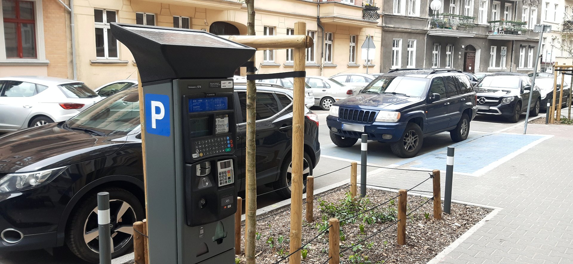 Zdjęcie przedstawia zaparkowane samochody oraz parkomat. - grafika artykułu