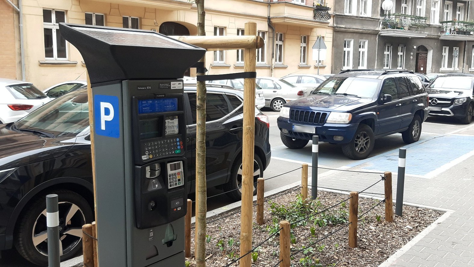 Zdjęcie przedstawia zaparkowane samochody oraz parkomat.