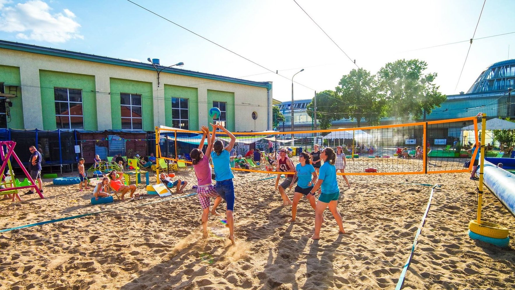 Zdjęcie przedstawia ludzi grających w siatkówkę plażową.