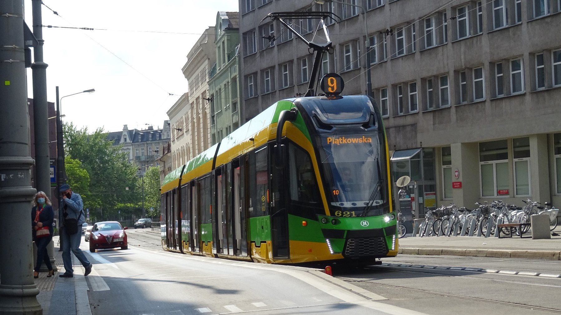 Tramwaj na przystanku wiedeńskim, w tle wysoki budynek, na przystanku dwoje ludzi