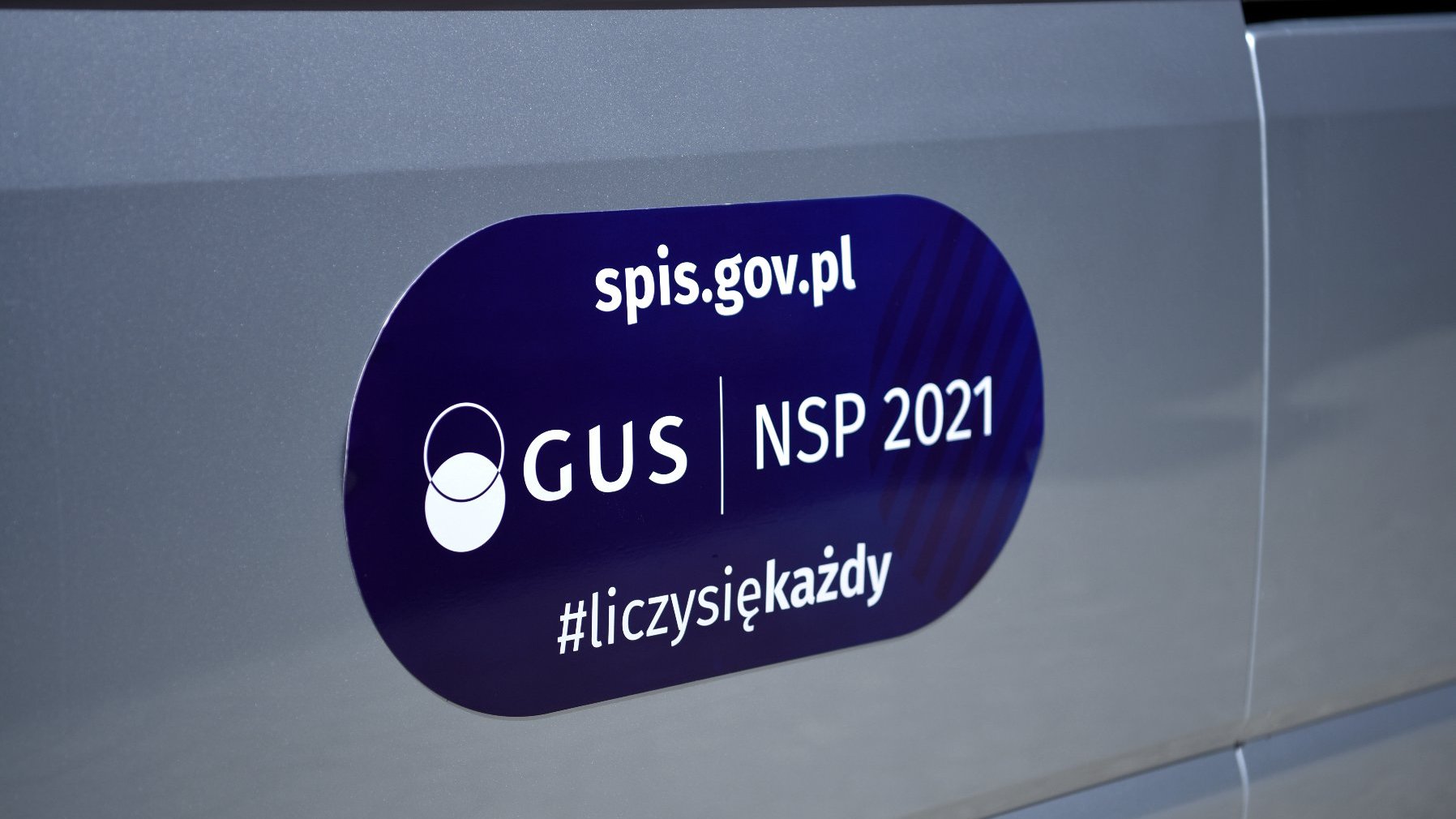 Zbliżenie na dzwi samochodu z niebieską naklejką "Narodowy Spis Powszechny".