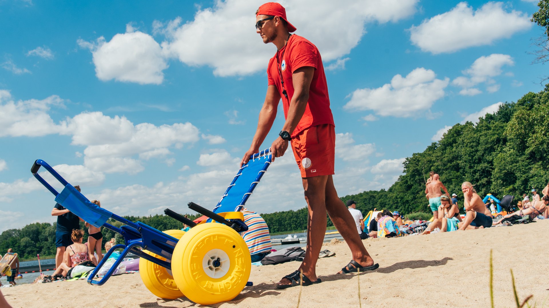 Zdjęcie przedstawia ratownika z wózkiem na plaży. Pcha on przed sobą wózek amfibie. - grafika artykułu