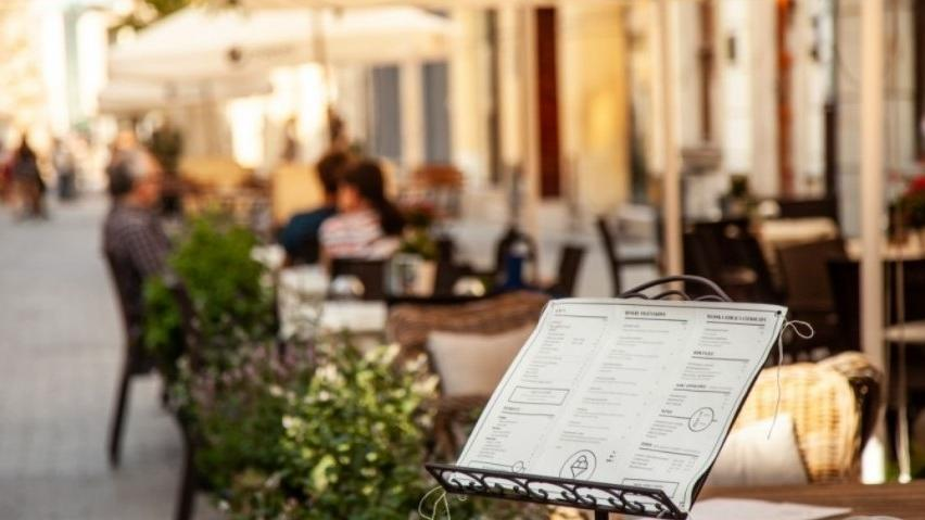 Na zdjęciu ogródek gastronomiczny, na pierwszym planie wystawione menu, w tle nieostre stoliki - grafika artykułu