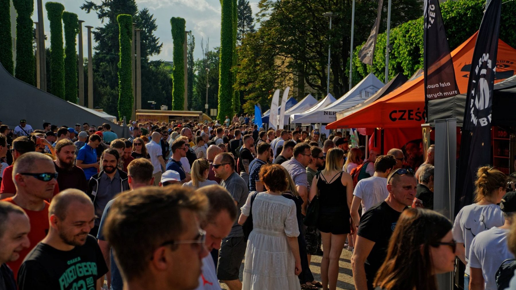 Zdjęcie przedstawia uczestników festiwalu. Po bokach namioty.