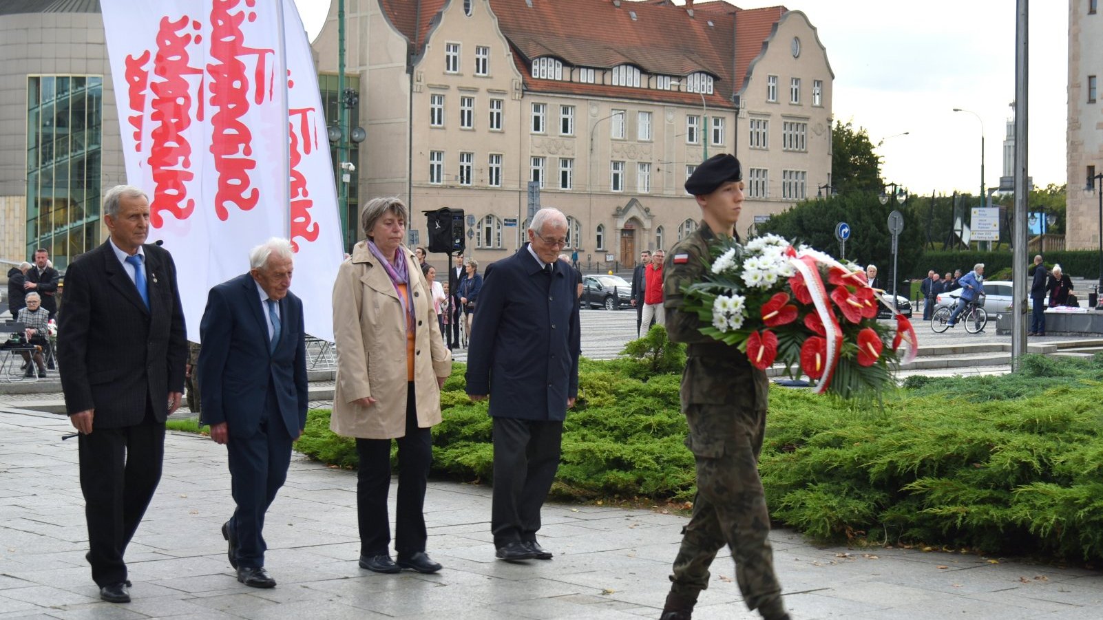 Zdjęcie przedstawia ludzi składających kwiaty.