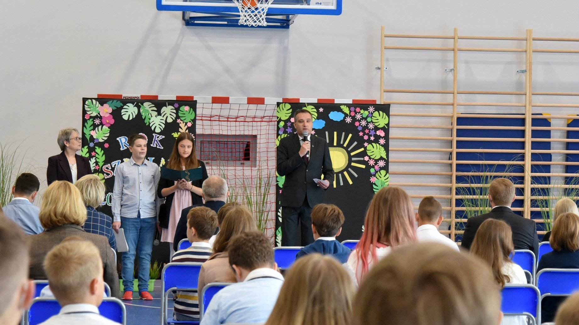 Zdjęcie przedstawia wiceprezydenta Wiśniewskiego z mikrofonem oraz słuchających go uczniów na sali gimnastycznej.