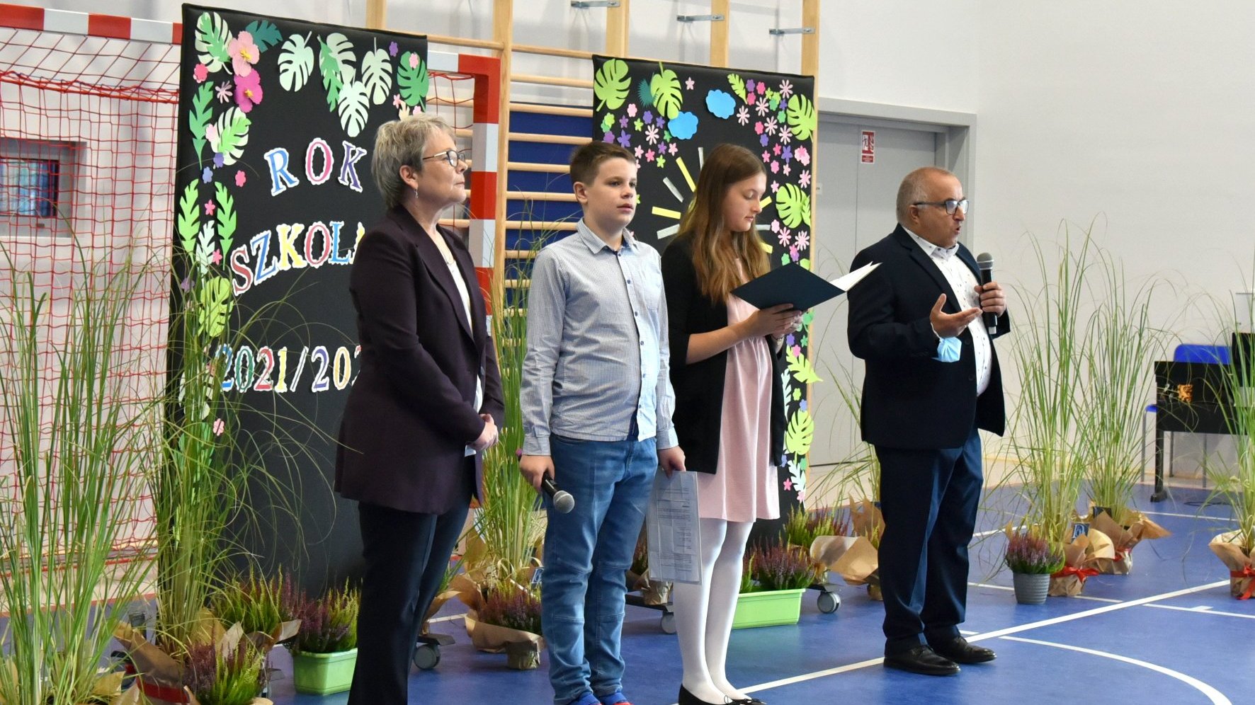 Zdjęcie przedstawia radnego Sternalskiego z mikrofonem. Obok stoją uczniowie i dyrektorka szkoły.