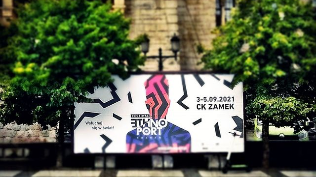 Zdjęcie przedstawia plakat Festiwalu Ethno Port stojący na chodniku przed Centrum Kultury Zamek.