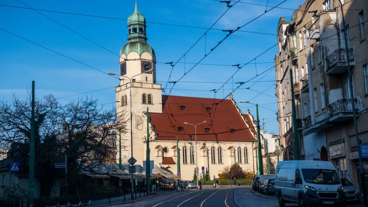 Zdjęcie przedstawia budynki i tory tramwajowe.